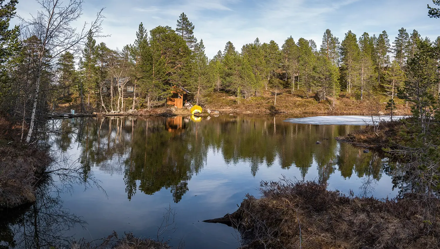 Calm mountain lake at Frystetjørn with a cabin among the pine trees and a yellow canoe by the shore – a peaceful nature getaway in Hardanger.