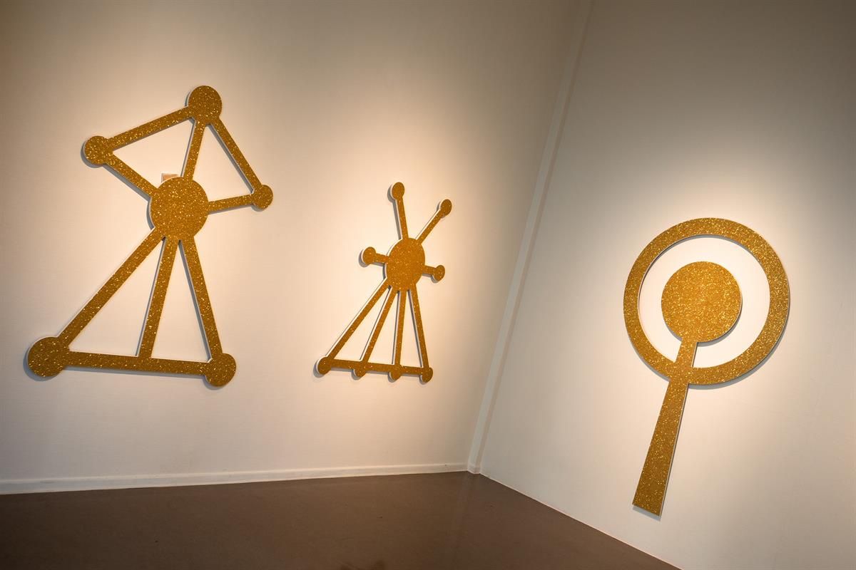 Yellow wall sculptures with graphic, symbolic shapes in an exhibition space.