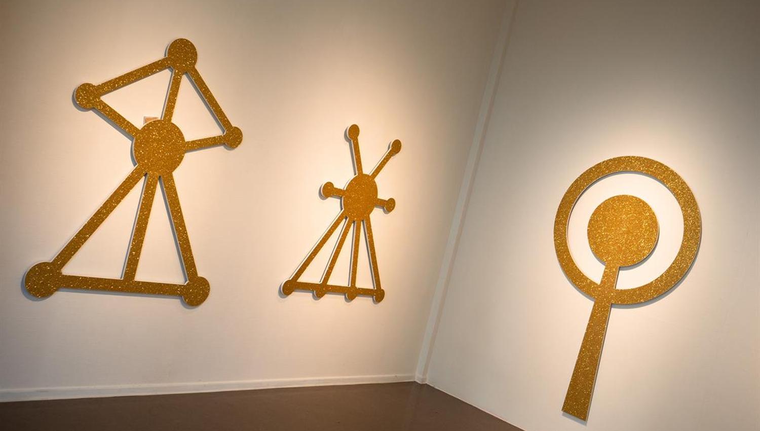 Yellow wall sculptures with graphic, symbolic shapes in an exhibition space.