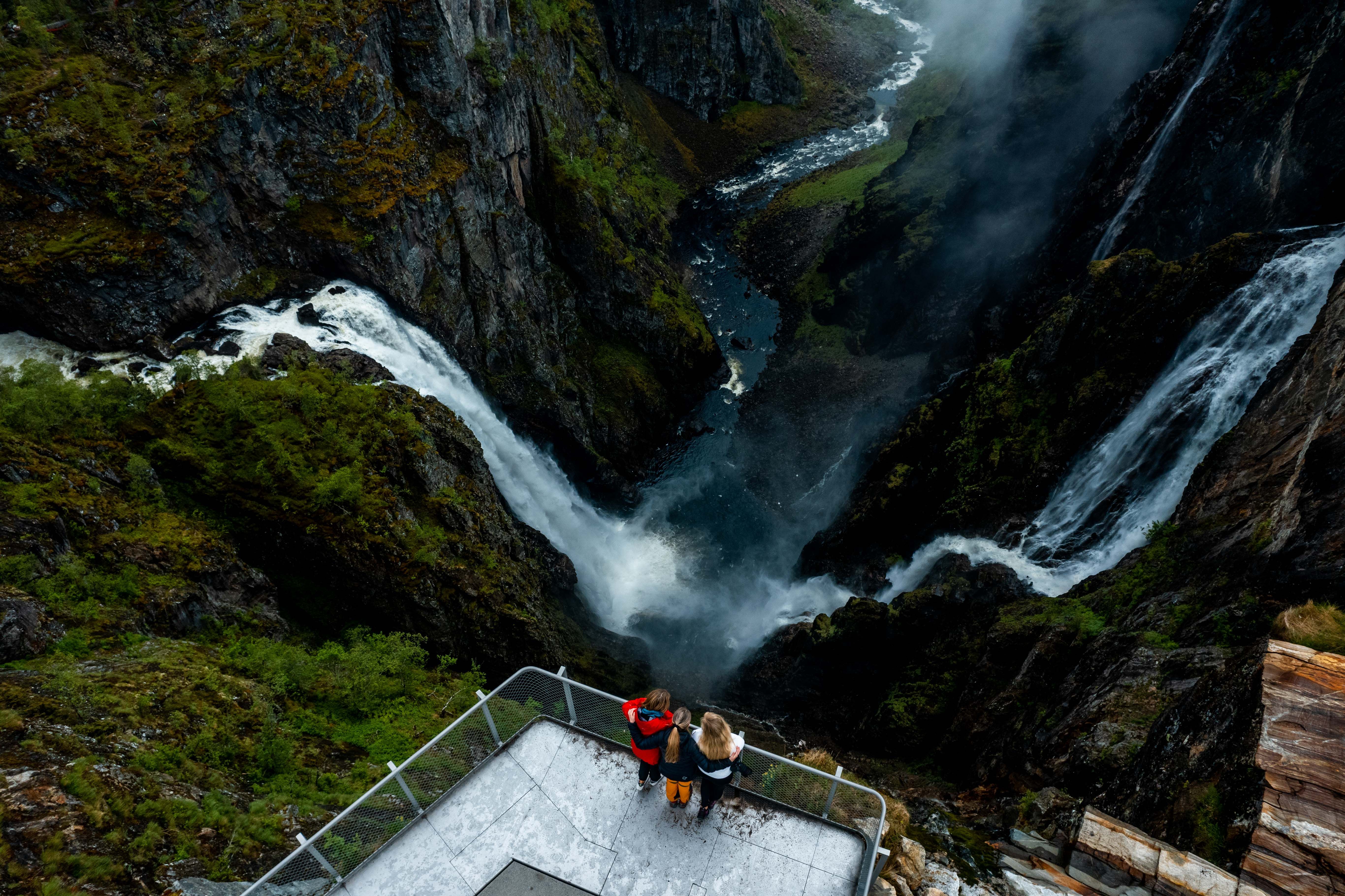 A drone shot where you see three persons on the viewing platform above the waterfall.