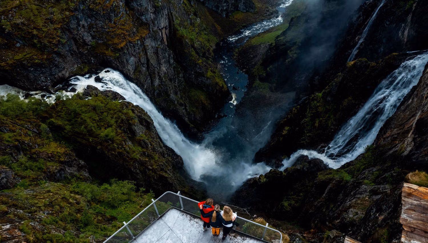 A drone shot where you see three persons on the viewing platform above the waterfall.