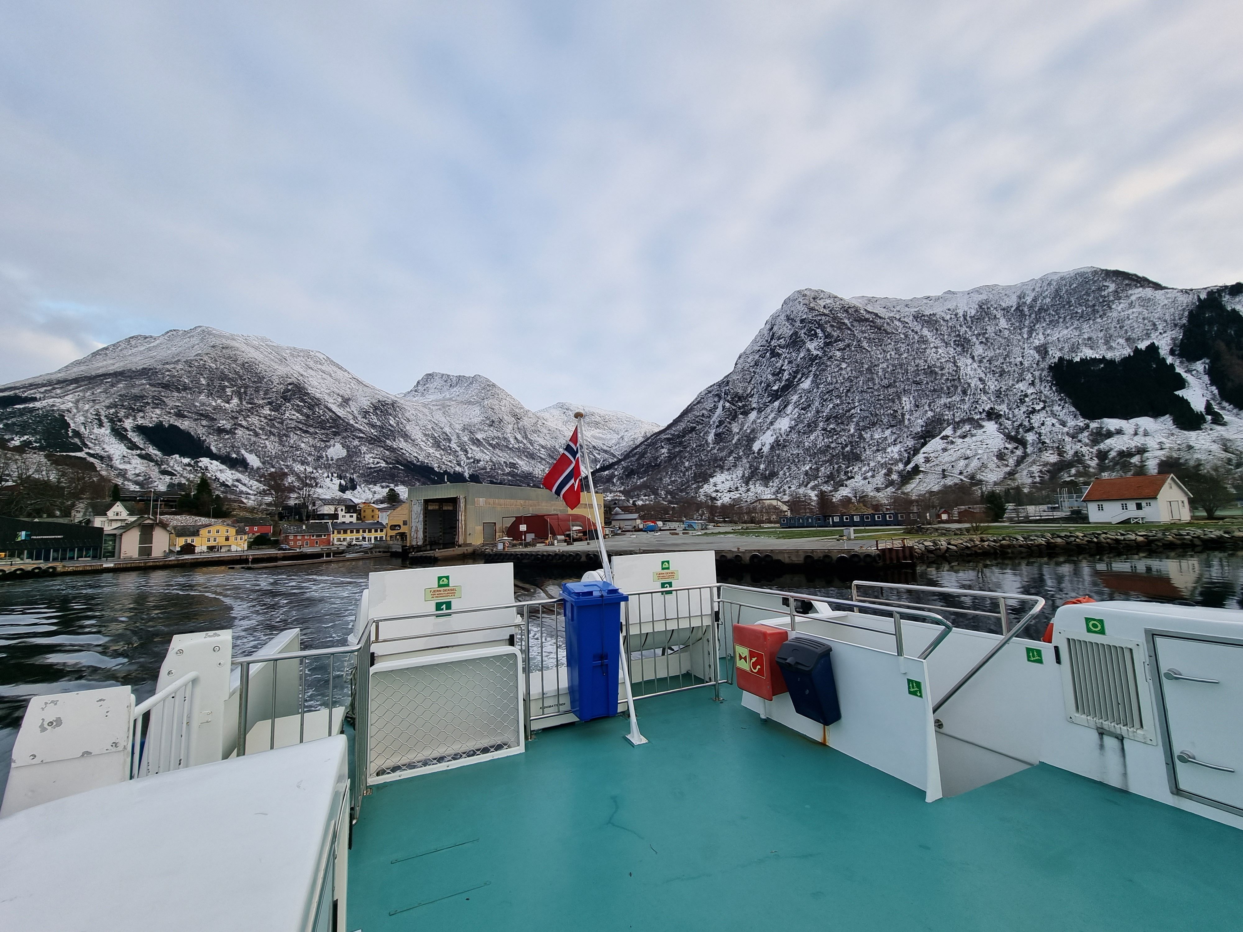 View from Hardangerfjordekspressen towards snow-covered mountains and small villages along the fjord.