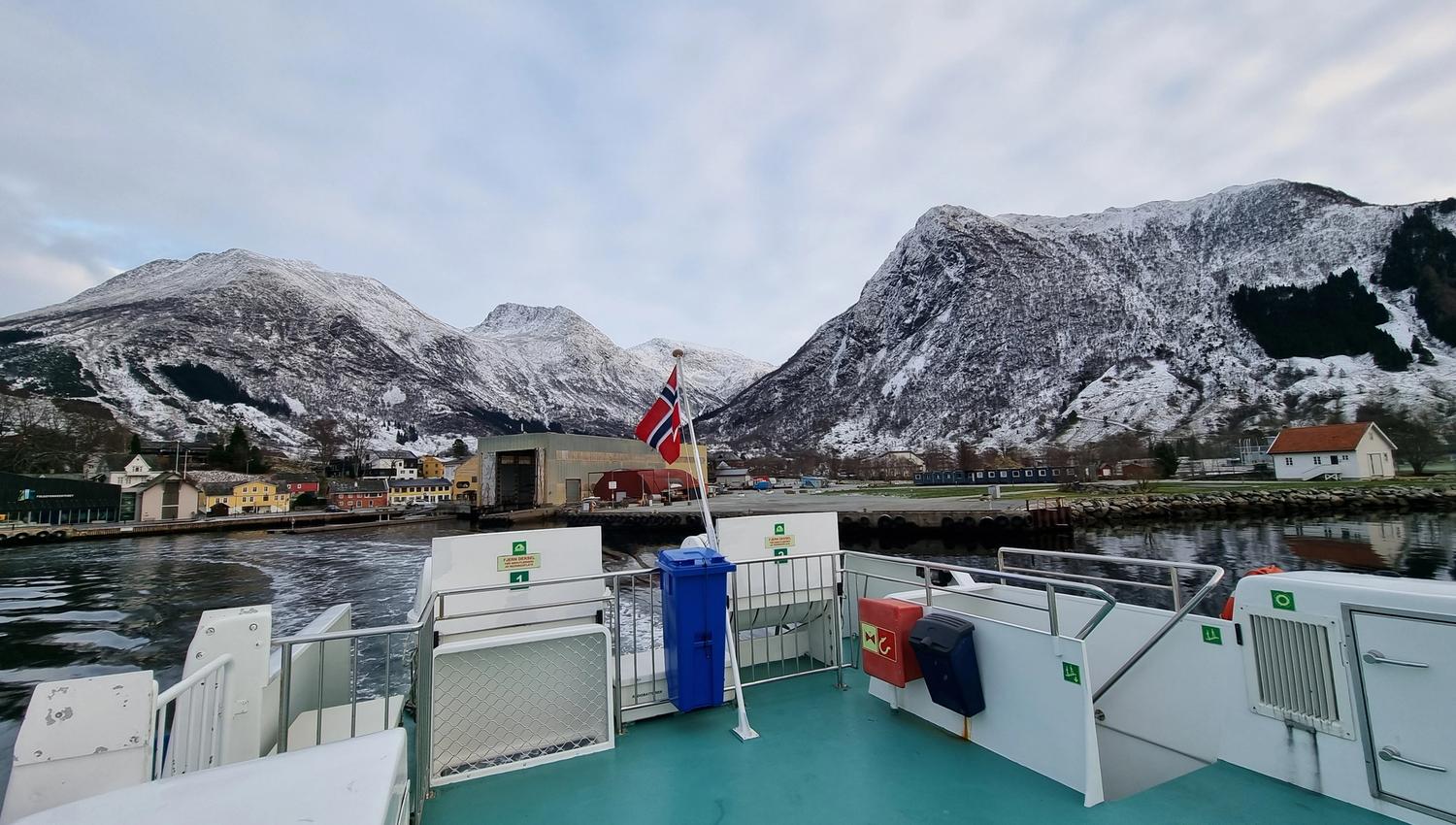 View from Hardangerfjordekspressen towards snow-covered mountains and small villages along the fjord.
