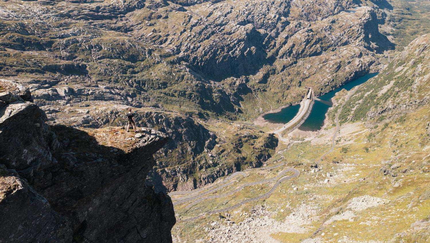 Person står på en massiv fjelltopp og ser utover fjellandskapet.
