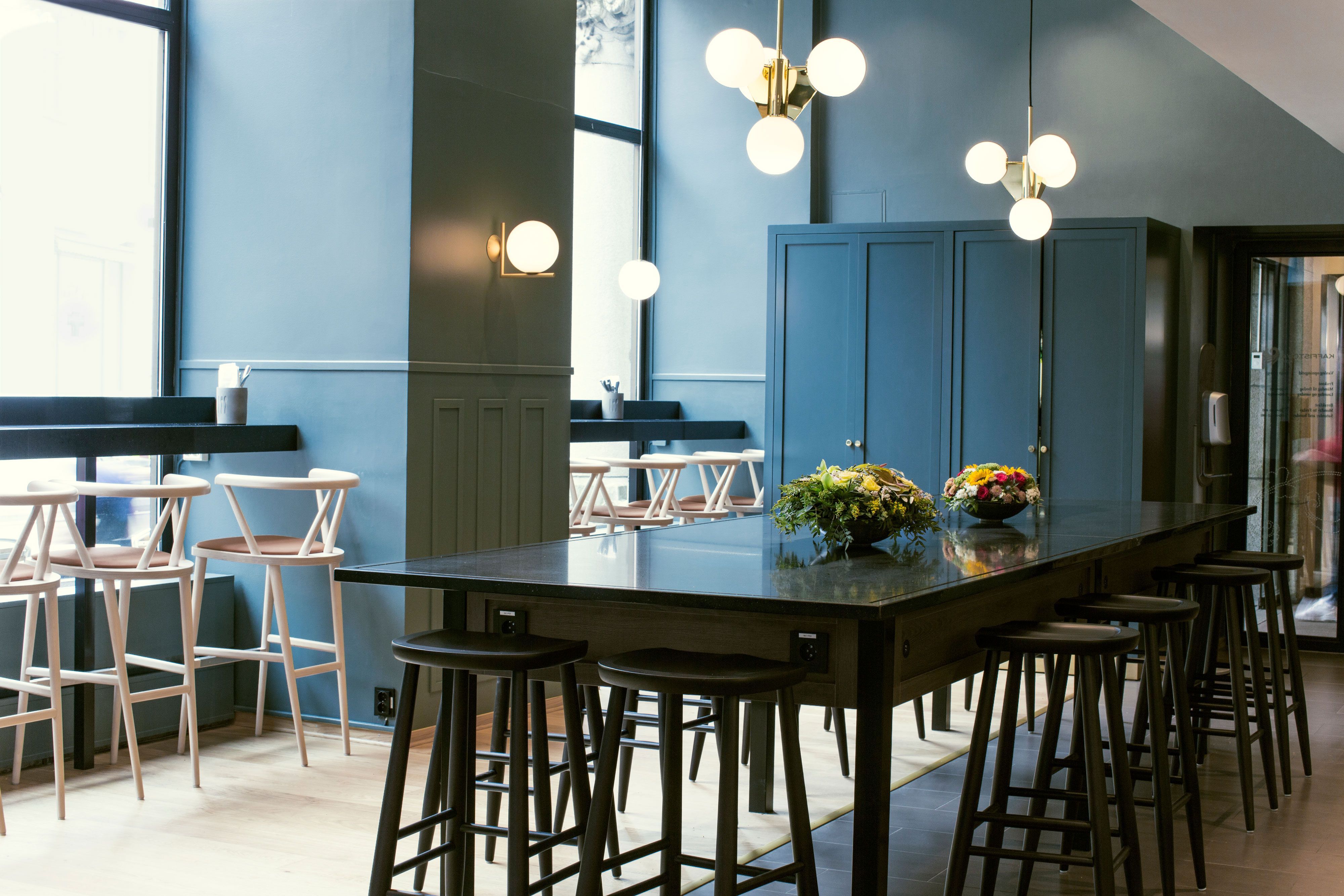 Black long table with bar stools, blue walls, round ceiling lamps.