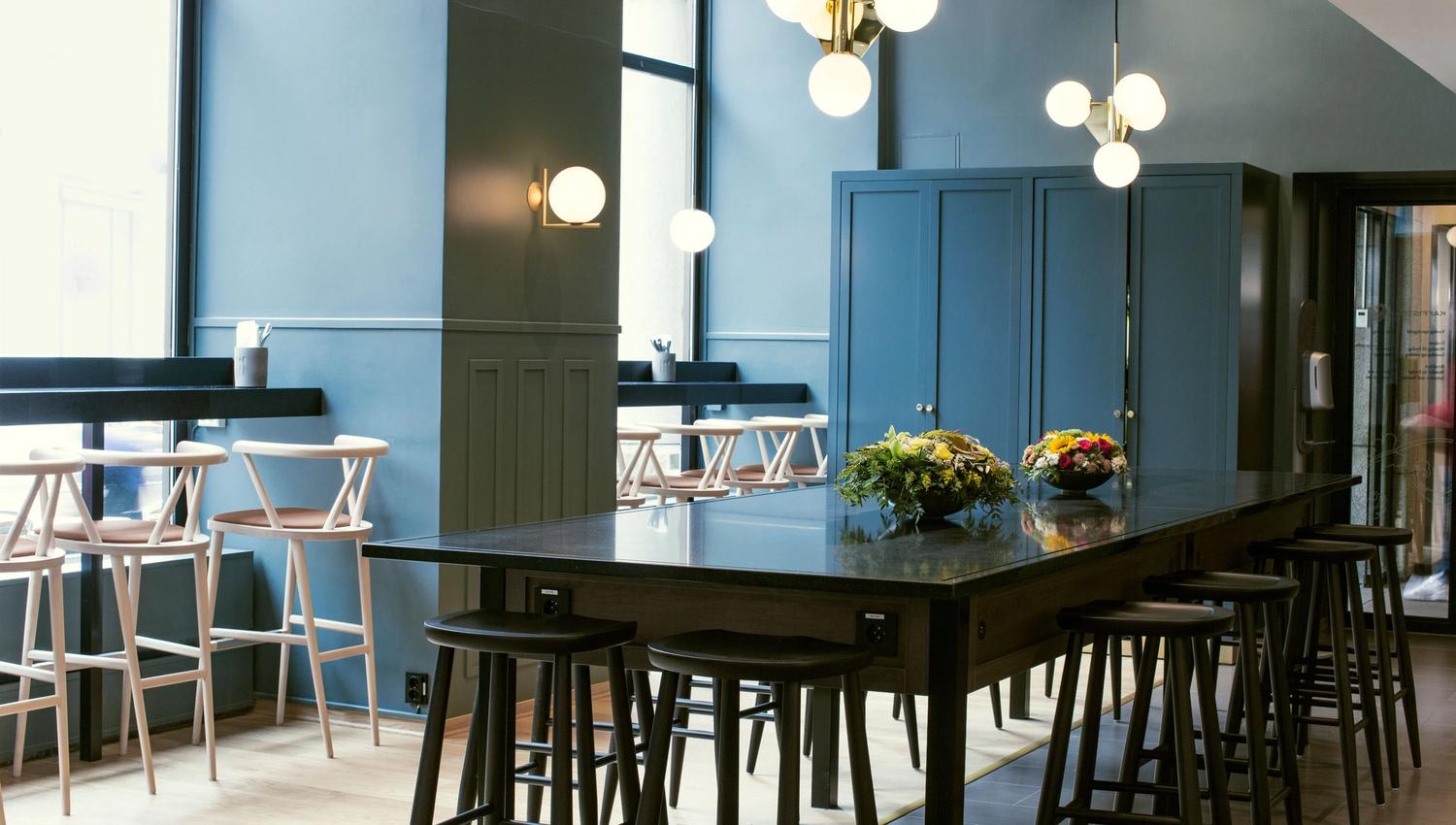 Black long table with bar stools, blue walls, round ceiling lamps.