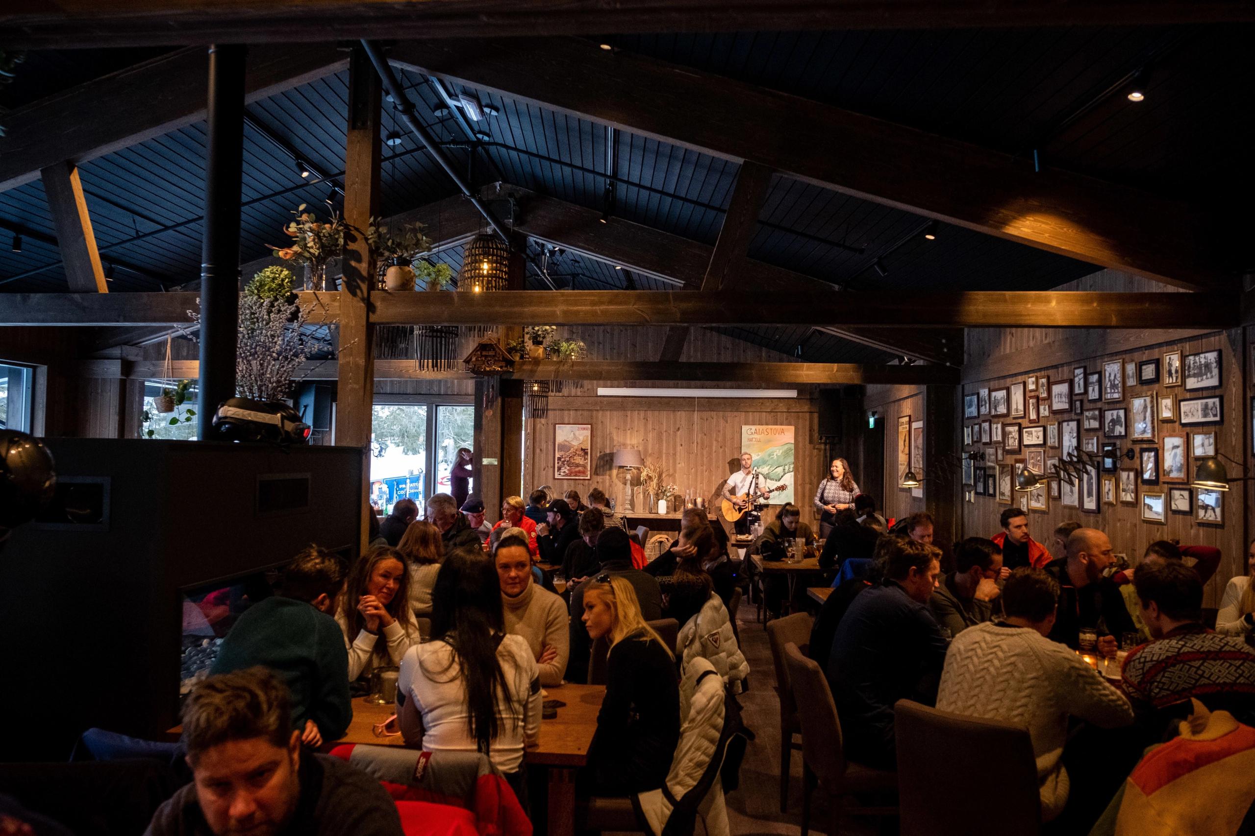 Fullsatt kafé i en treinnredet sal med publikum ved bord, mens to musikere spiller på en liten scene..