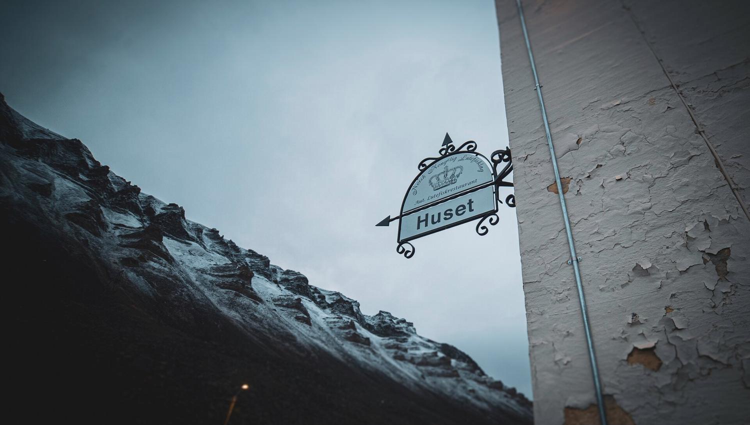 Et skilt ved inngangsdøren til Huset med fjell i bakgrunnen
