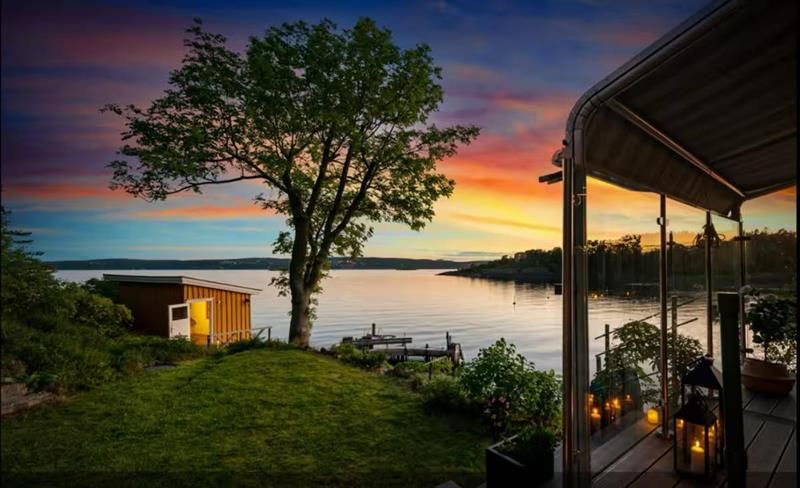 A peaceful evening by the sea with a view over the water, a tree, and a lit cabin at sunset.