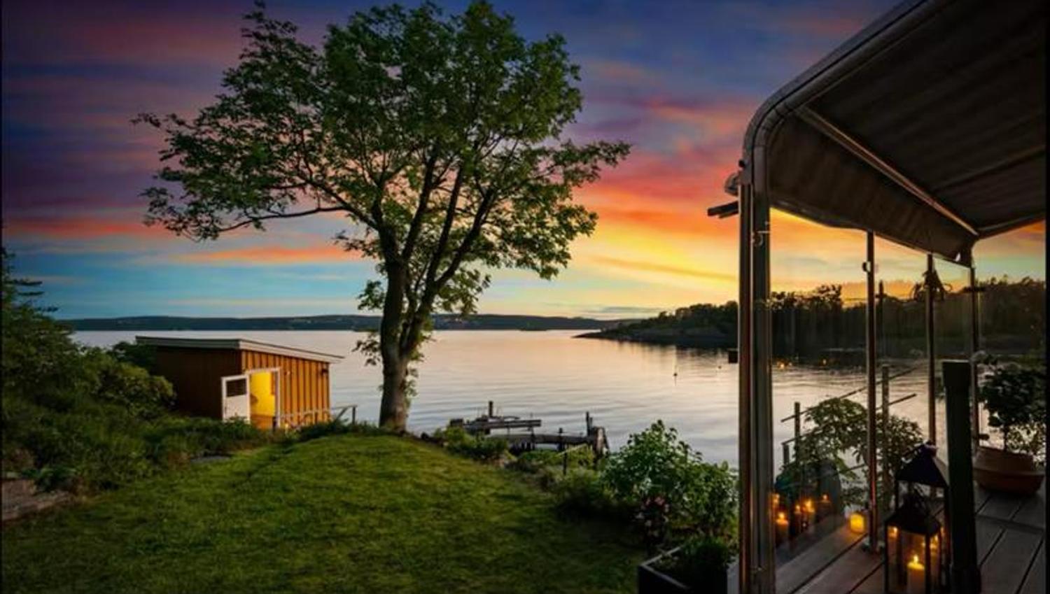 A peaceful evening by the sea with a view over the water, a tree, and a lit cabin at sunset.