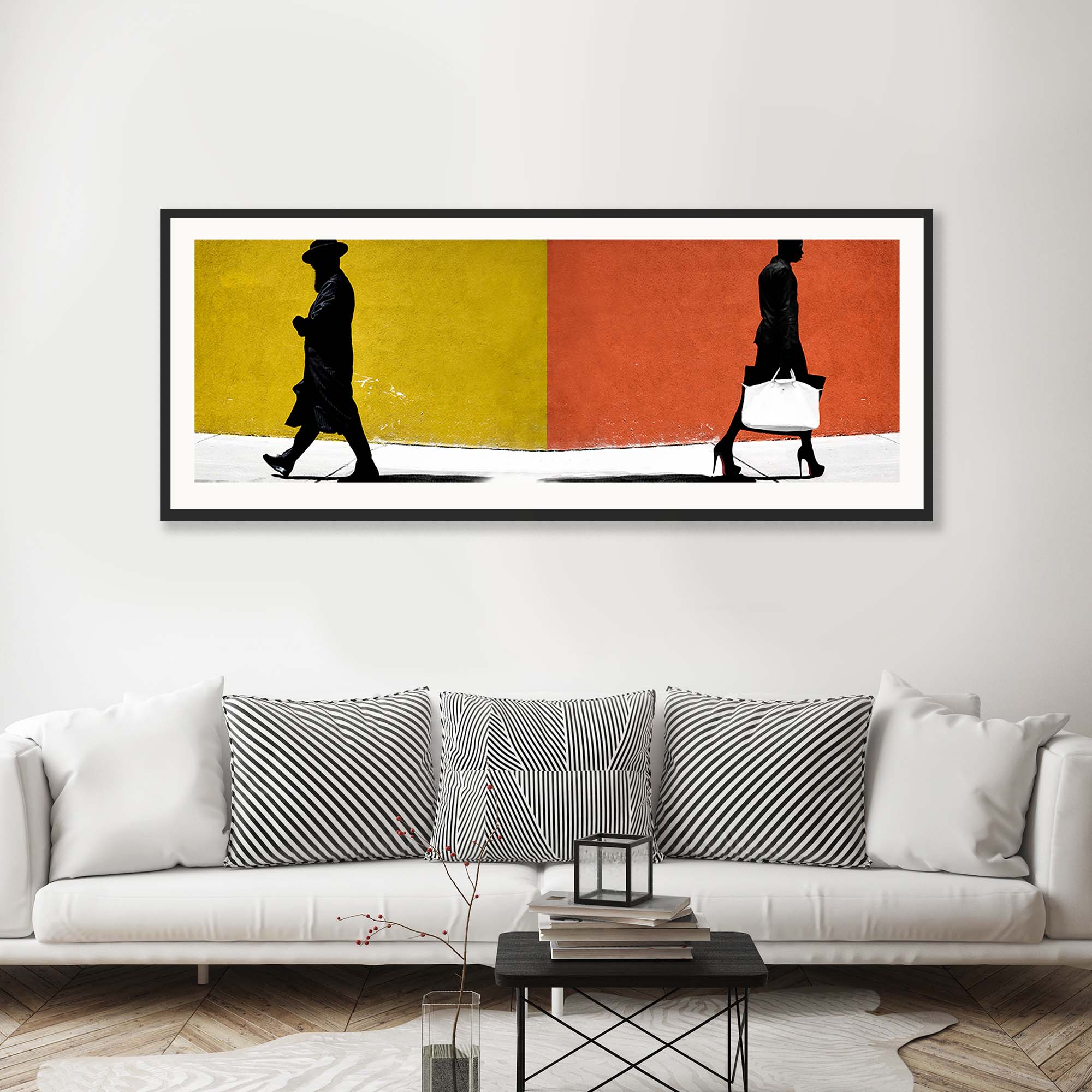 Grå sofa og svart bord med et langt bilde med orange og gule farger og en mann gående