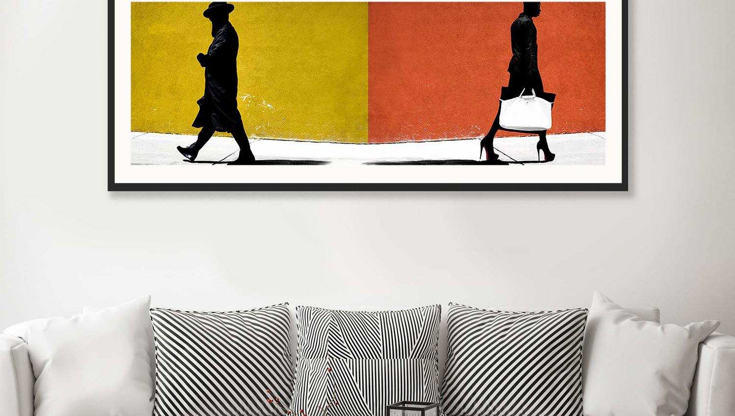 Grå sofa og svart bord med et langt bilde med orange og gule farger og en mann gående