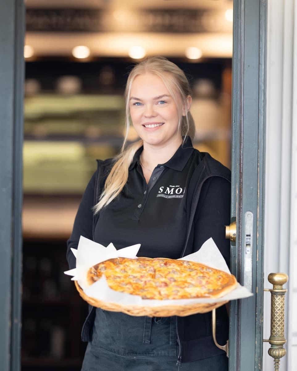 Smiling waiter from SMOI standing in the doorway holding a delicious pizza