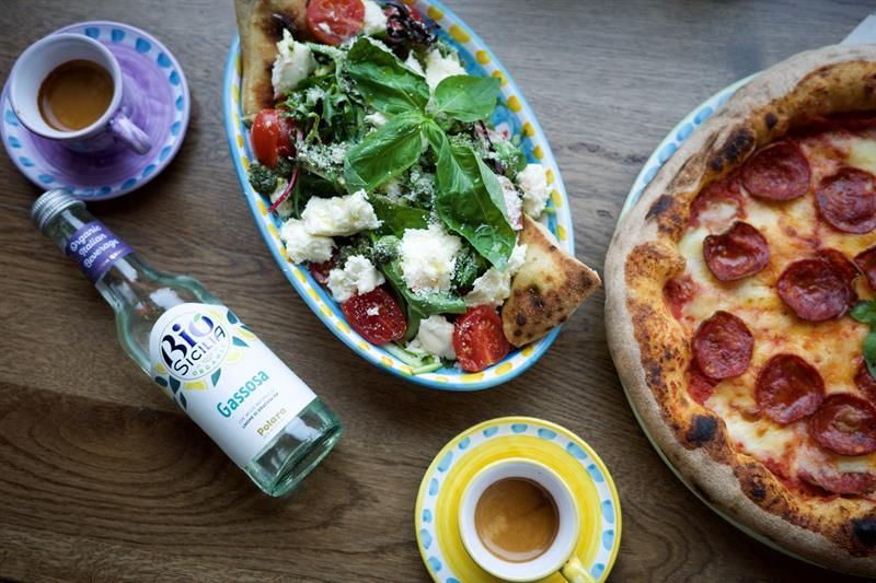 Detail of pizza, salad, two coffee cups and a bottle of Italian lemonade