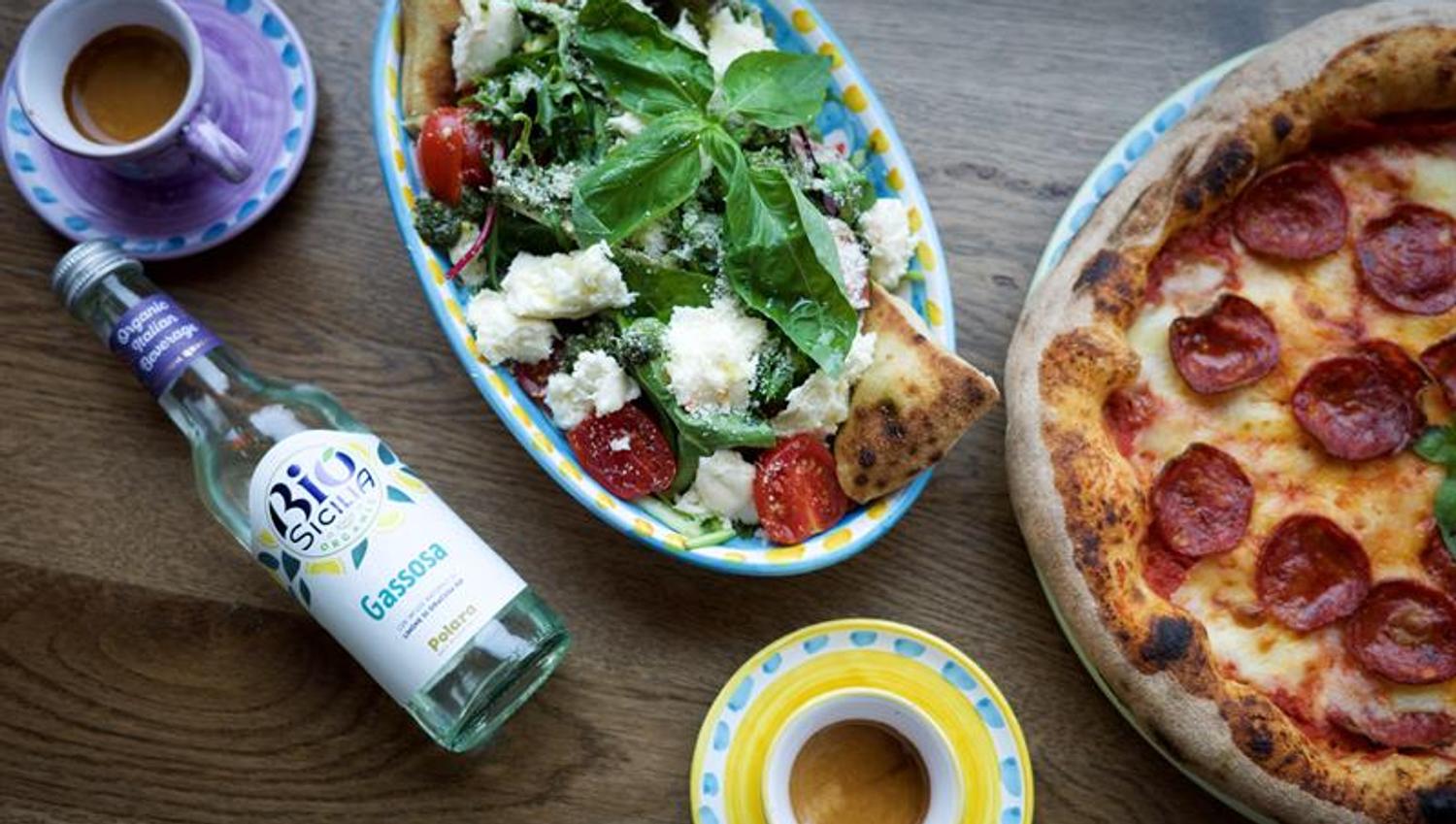 Detail of pizza, salad, two coffee cups and a bottle of Italian lemonade