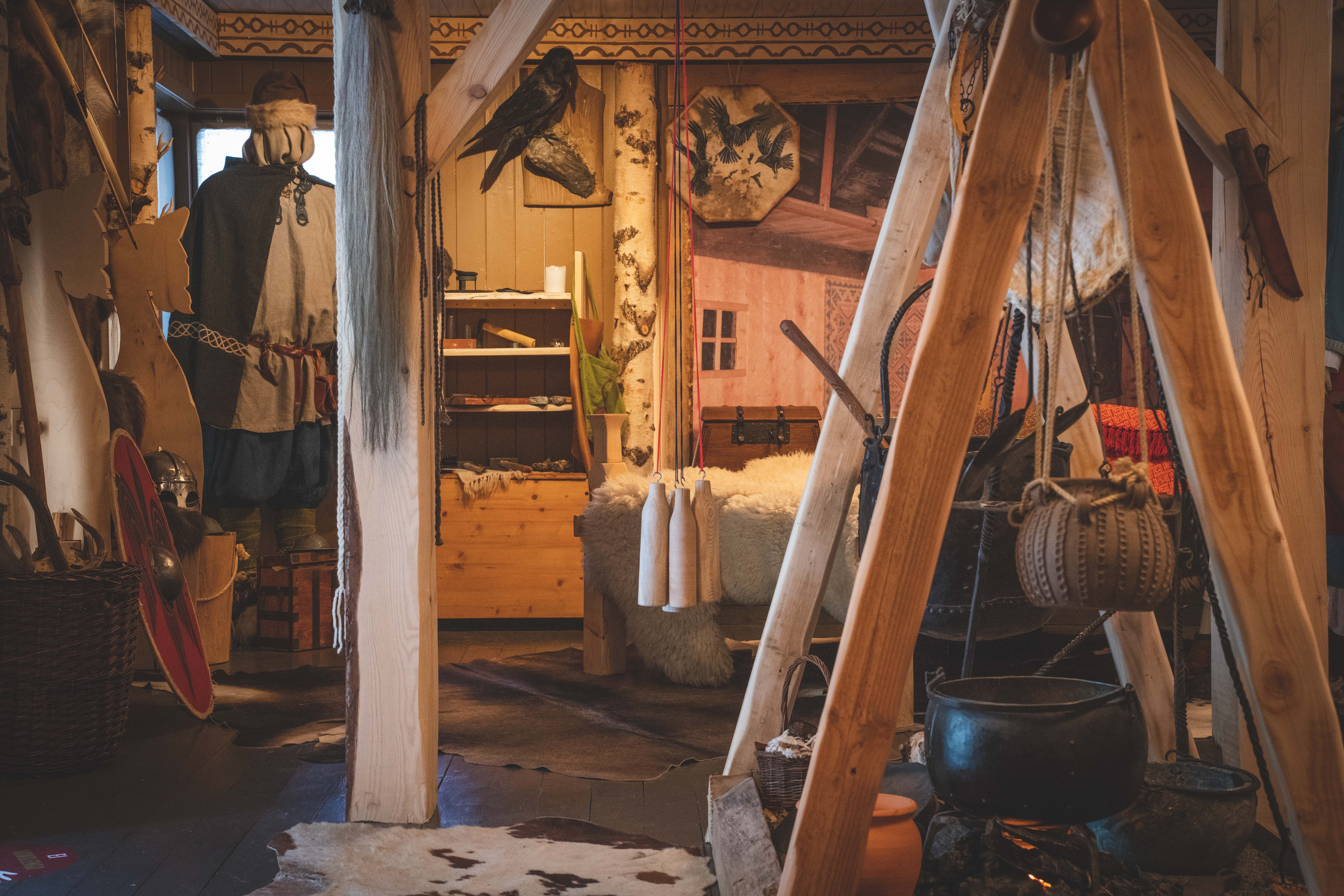In der Wikingerausstellung sind ein Schild, eine Schaufensterpuppe in Wikingerkleidung, ein Bett mit Schaffellen, ein an der Wand hängendes Rentierfell und ein auf einem Holzständer über einer Feuerstelle montierter Wasserkocher zu sehen.