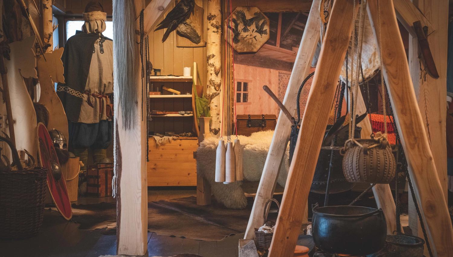 In der Wikingerausstellung sind ein Schild, eine Schaufensterpuppe in Wikingerkleidung, ein Bett mit Schaffellen, ein an der Wand hängendes Rentierfell und ein auf einem Holzständer über einer Feuerstelle montierter Wasserkocher zu sehen.