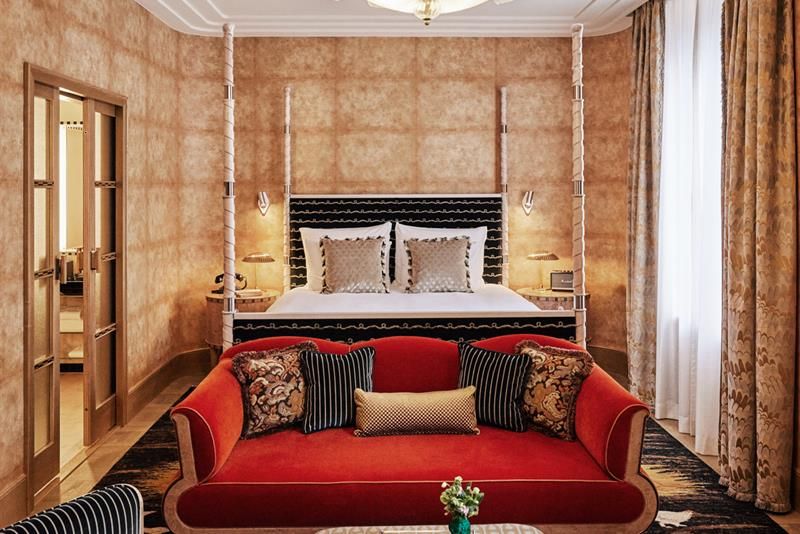 Hotel room with a large double bed behind red sofa