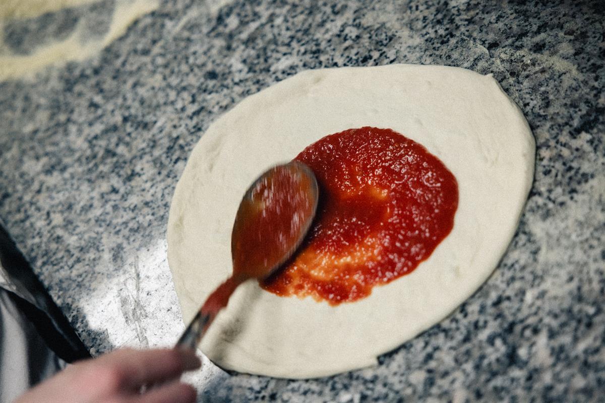 Tomato sauce being spread on pizza dough.