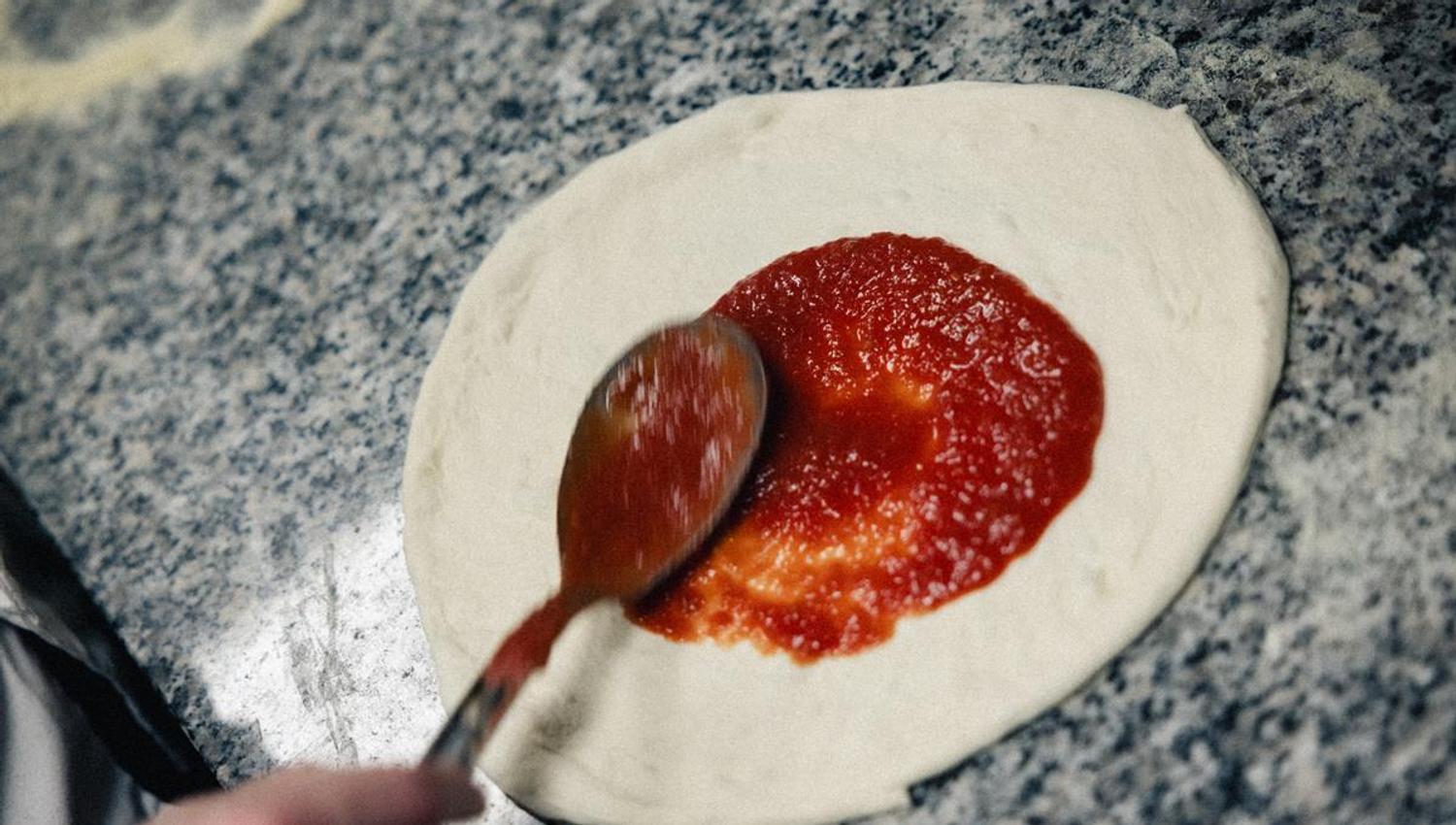 Tomato sauce being spread on pizza dough.