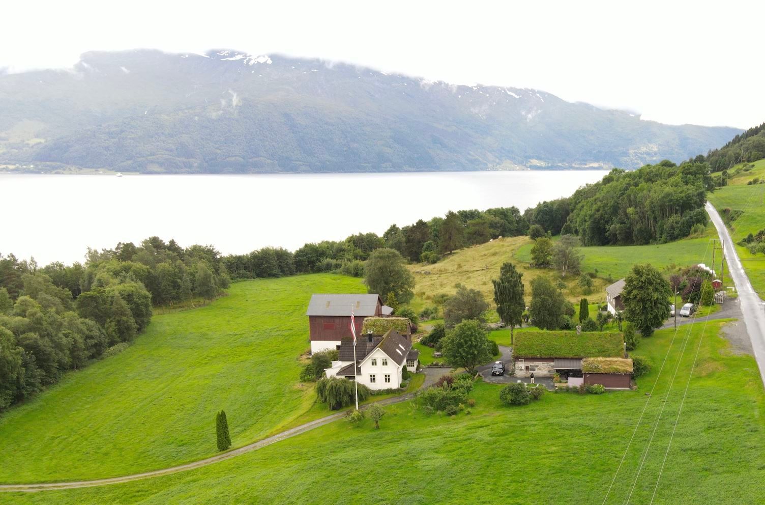 Orheimstunet in Nordfjord - A rural farmhouse and barns on green hills near a large lake, with forested mountains in the background..