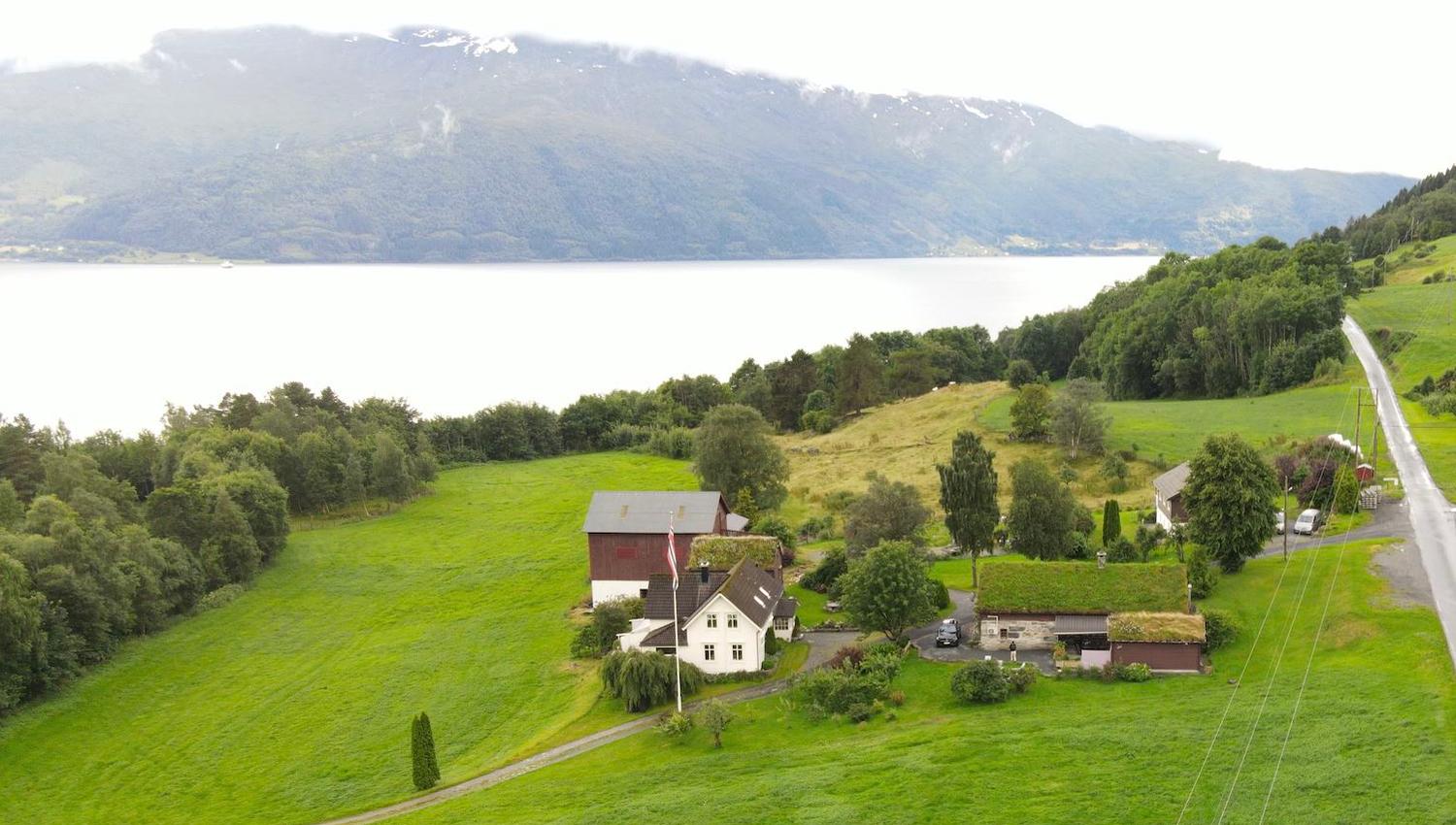 Orheimstunet in Nordfjord - A rural farmhouse and barns on green hills near a large lake, with forested mountains in the background..