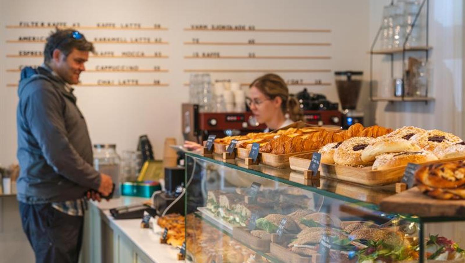 A man standing at the cashregister paying for some baked goods.
