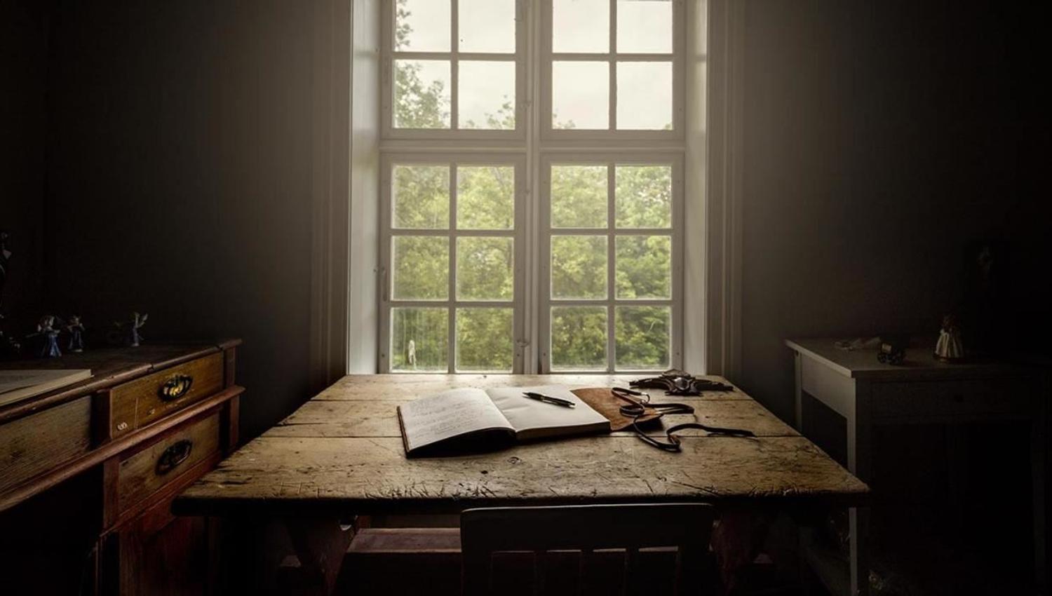 The library at Skrivergaarden with historic furniture, books and views through the window towards the garden and fjord.