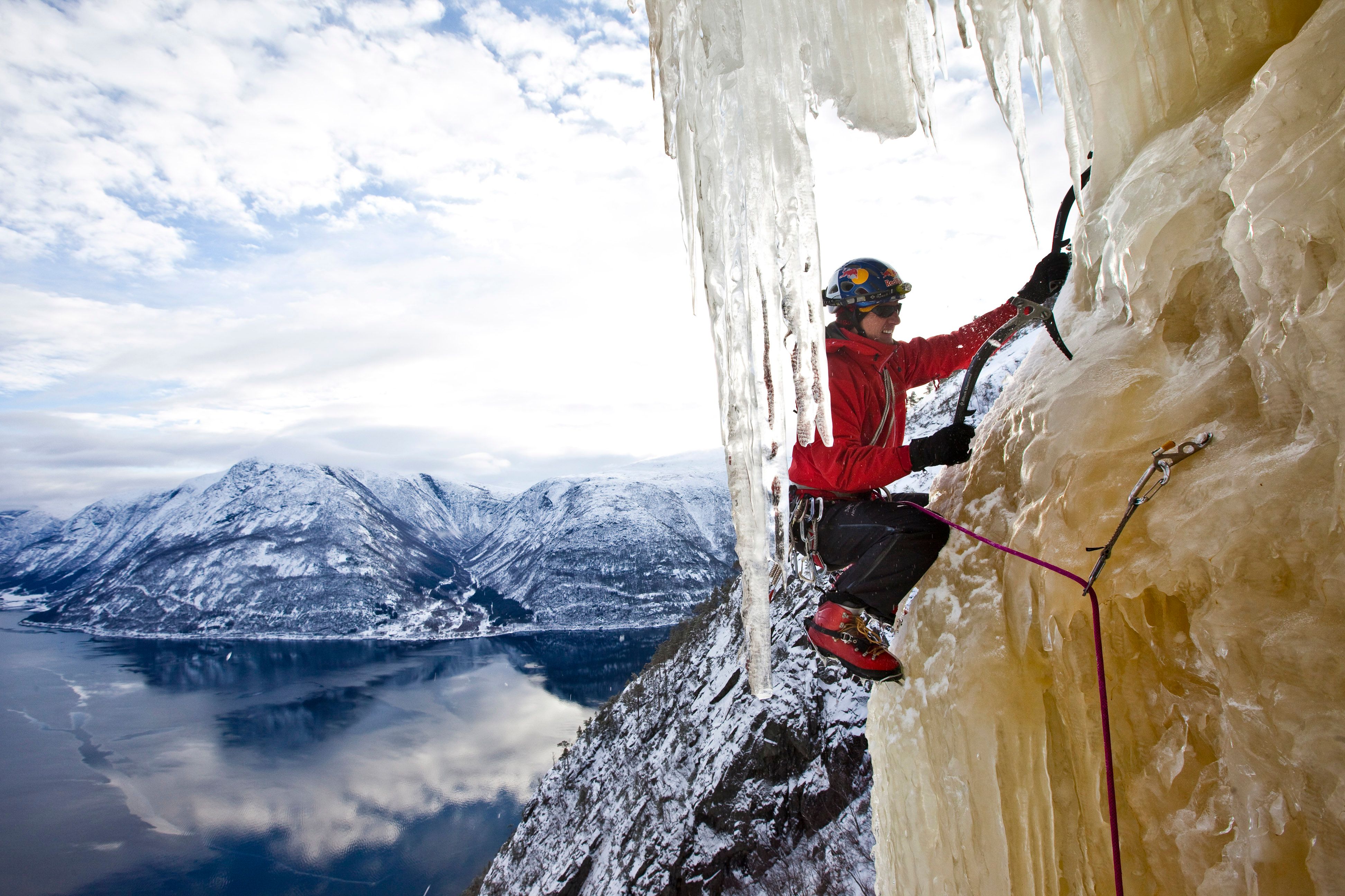 A side view of an iceclimber climbing the ice, with the fjord below.