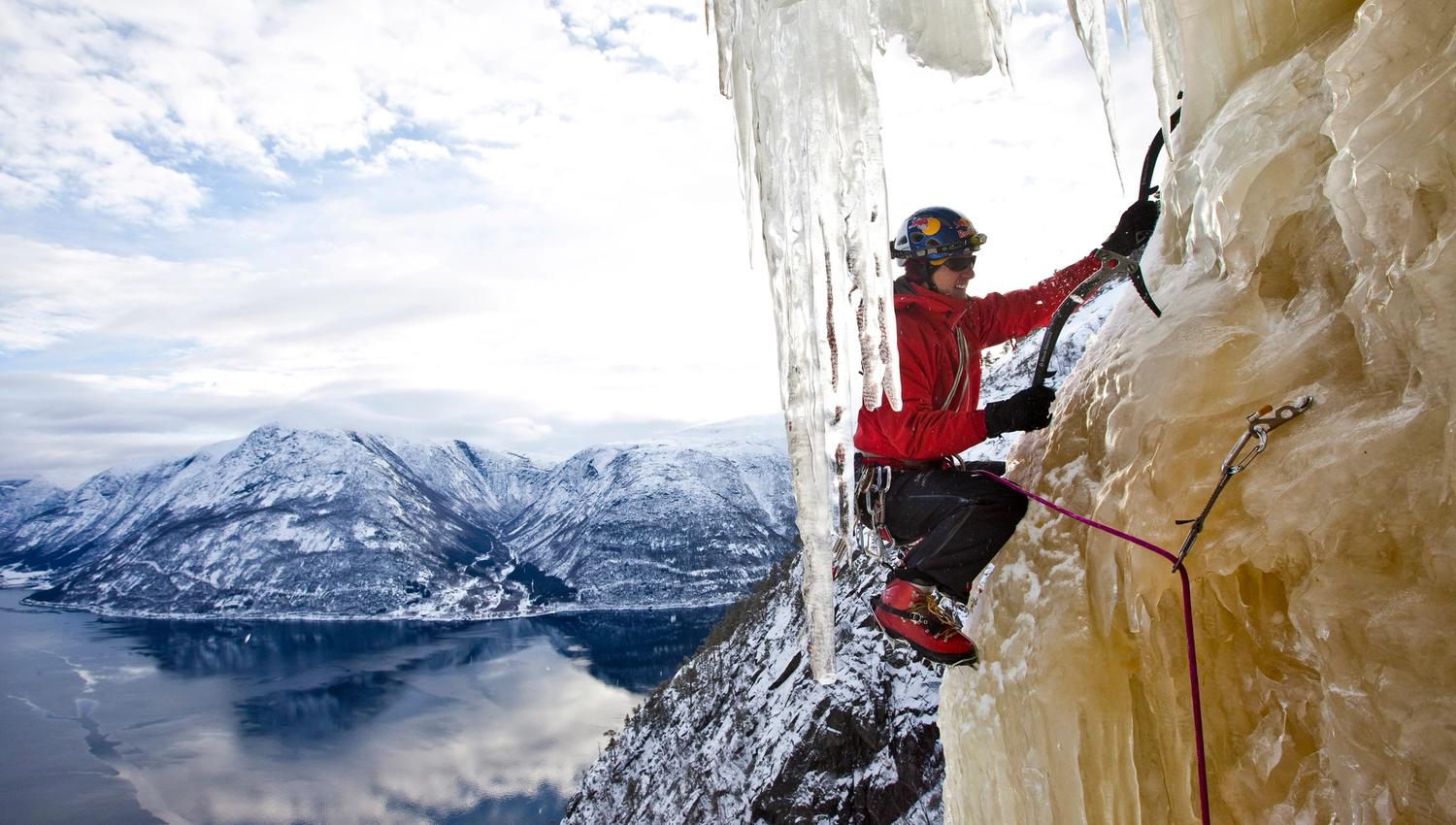 A side view of an iceclimber climbing the ice, with the fjord below.