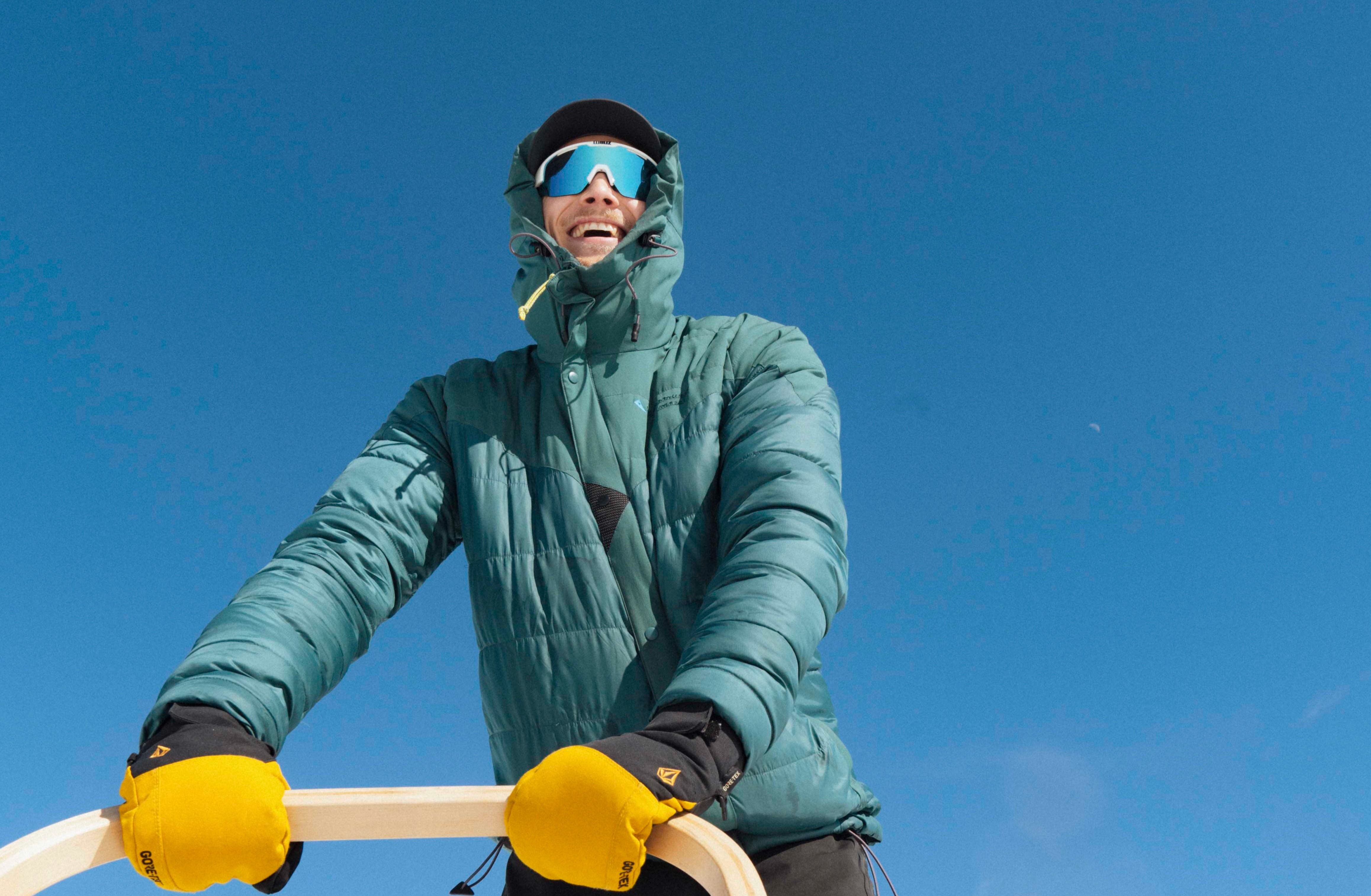 A person dressed in a warm jacket and yellow gloves is dogsledding on folgefonna husky camp.