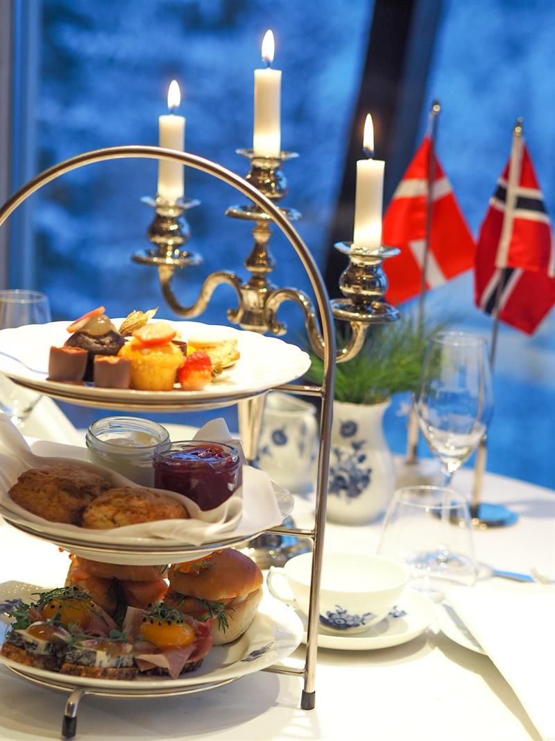 Elegant afternoon tea servert på et etasjefat med levende lys og norske flagg ved vinduet.