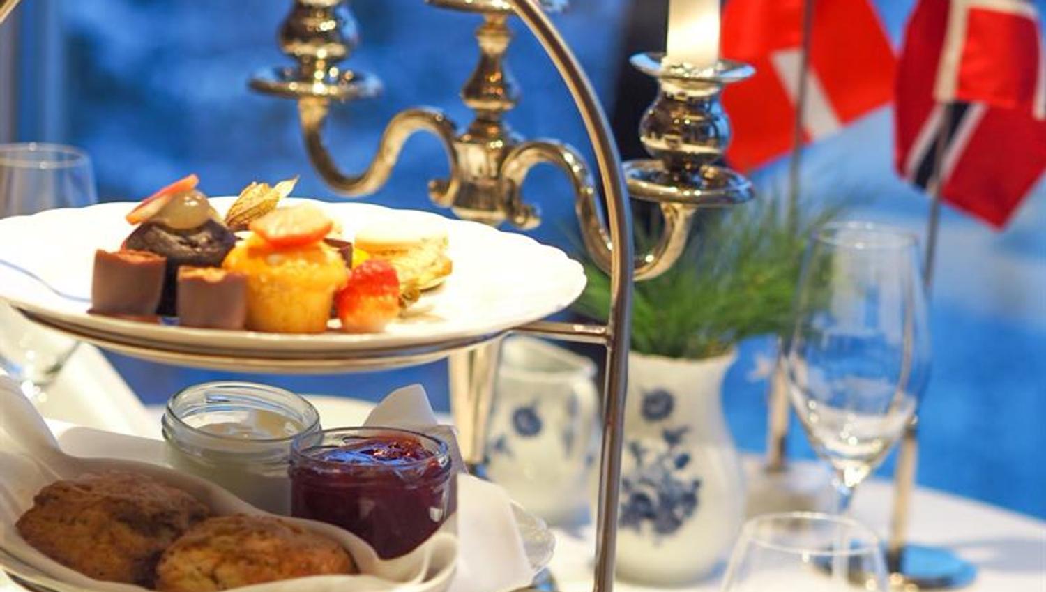Elegant afternoon tea servert på et etasjefat med levende lys og norske flagg ved vinduet.