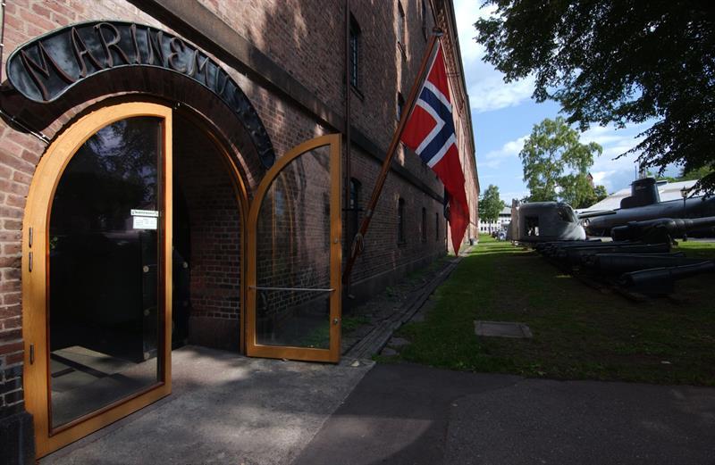 Open entrance to the Norwegian Naval Museum in Horten, with a Norwegian flag and historic naval vessels outside.