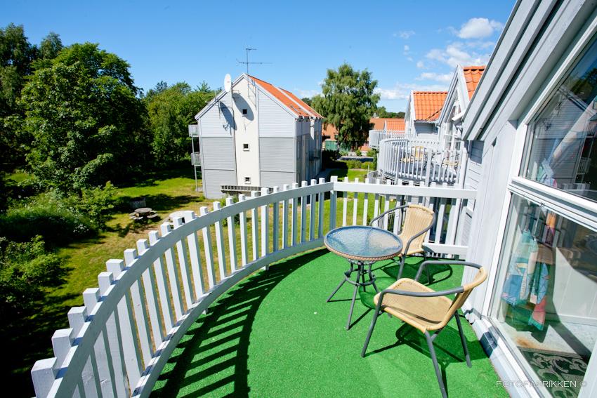 Small balcony with a white railing and artificial grass. Two mesh chairs and a small table.