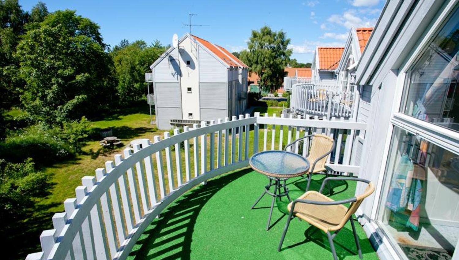 Small balcony with a white railing and artificial grass. Two mesh chairs and a small table.