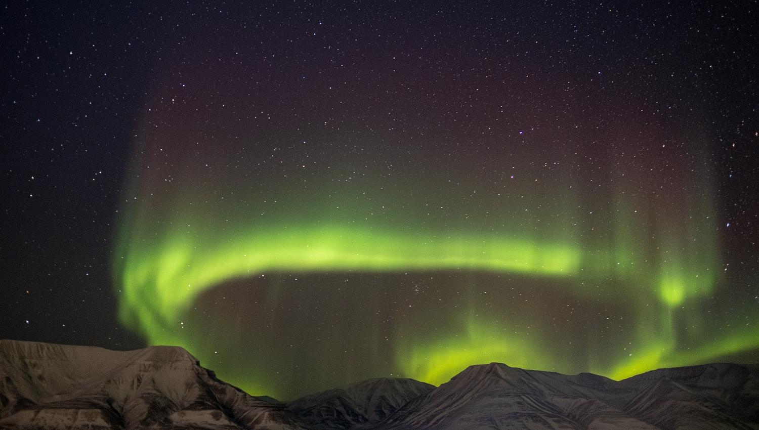 A circle of northern lights in the skies above a mountain range