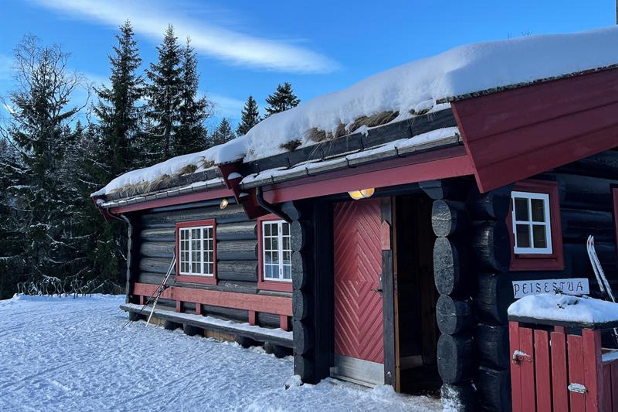Svart og rød hytte i marka. Blå himmel og snø på bakken