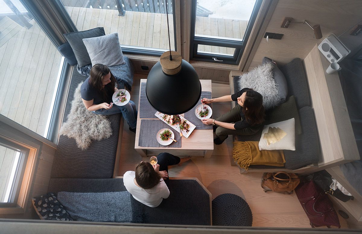 Image taken from above showing three persons around a table in a small living room with large windows