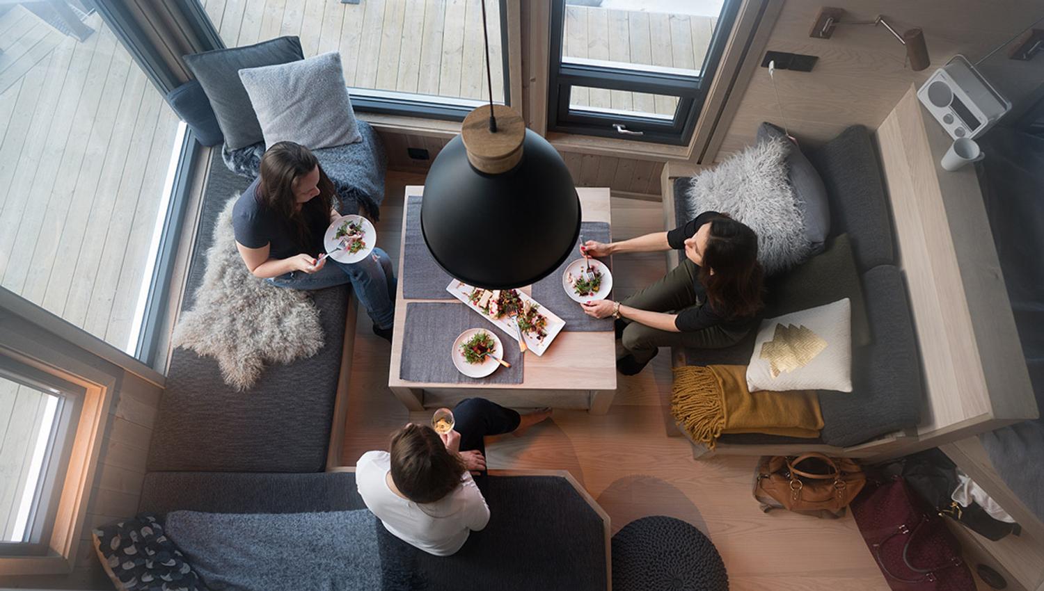 Image taken from above showing three persons around a table in a small living room with large windows