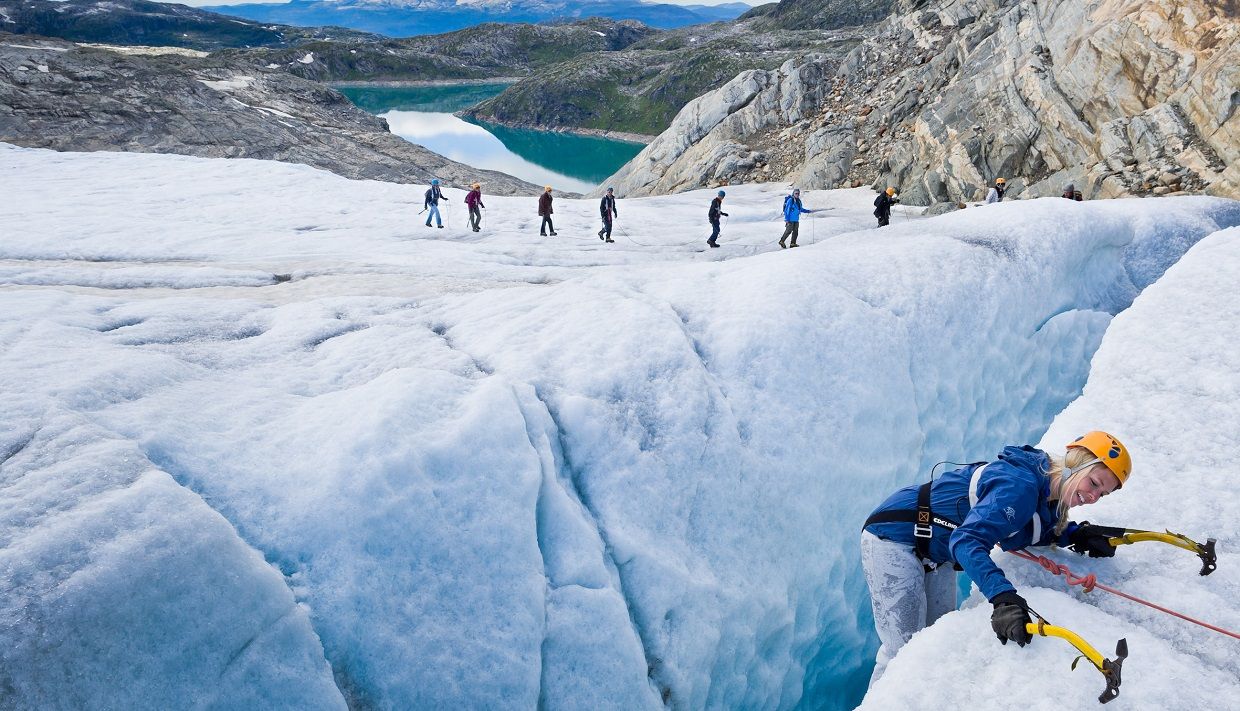 A glacier guide secures a participant climbing across a deep crevasse on the Folgefonna Glacier.