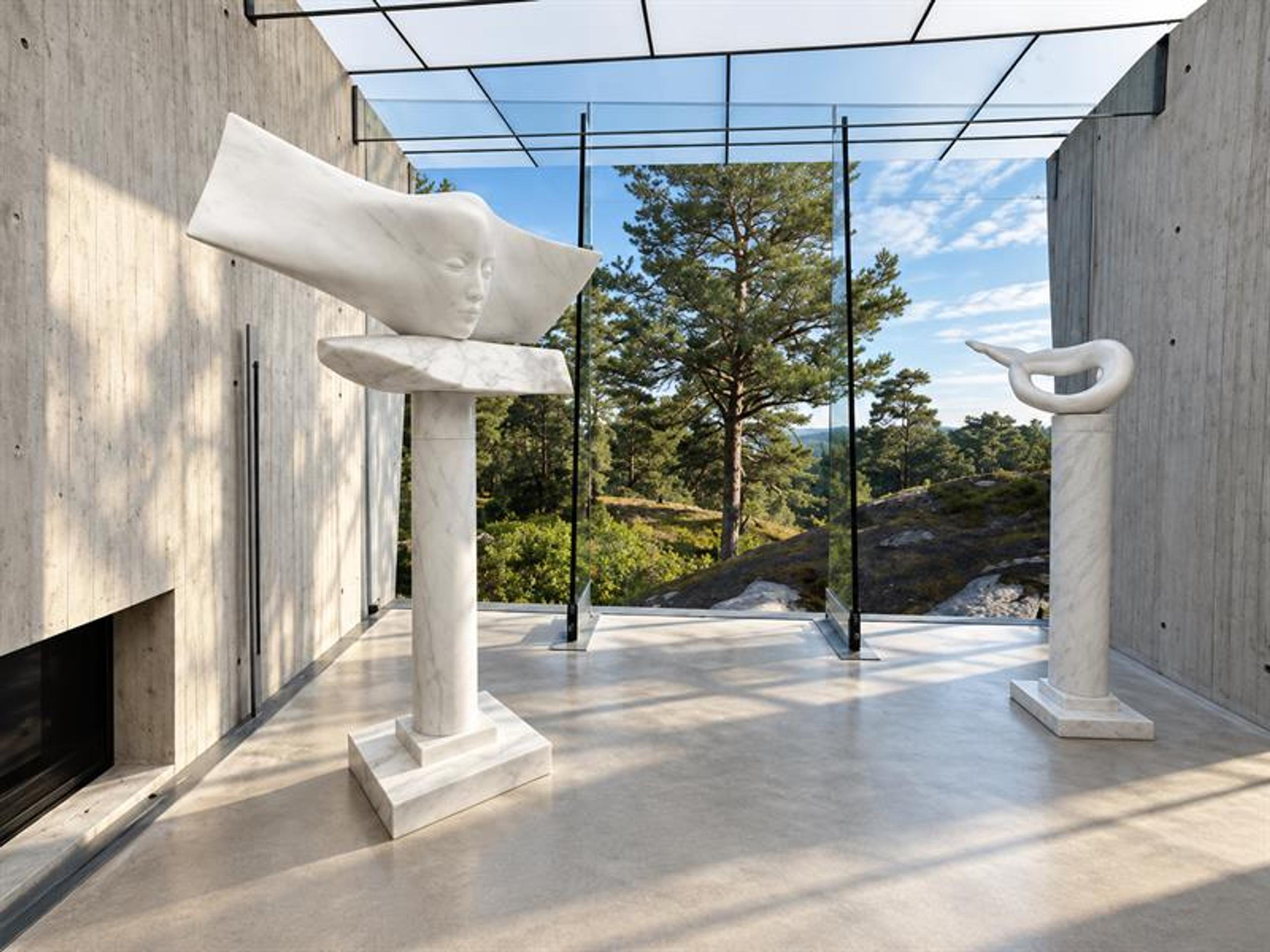 To hvite marmorskulpturer av Knut Steen i Midtåsen Skulpturpaviljong, med betongvegger og glassfasade mot skogen.