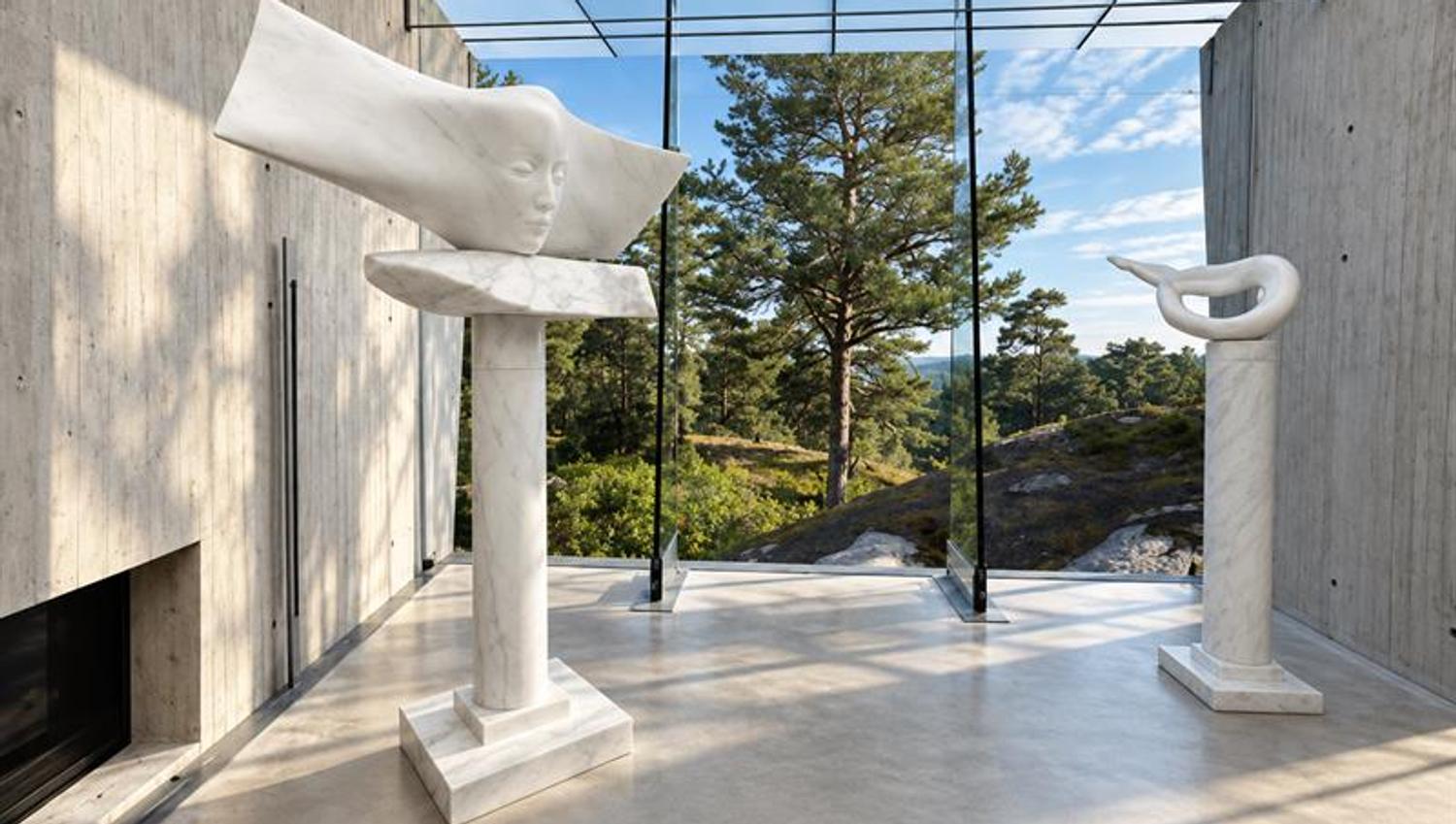 To hvite marmorskulpturer av Knut Steen i Midtåsen Skulpturpaviljong, med betongvegger og glassfasade mot skogen.