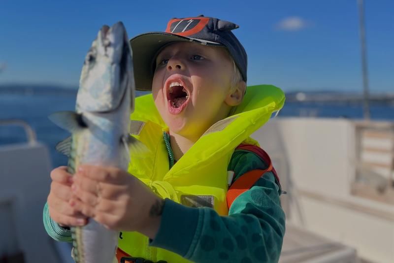 A child proudly holds up a fish they have just caught on the boat.