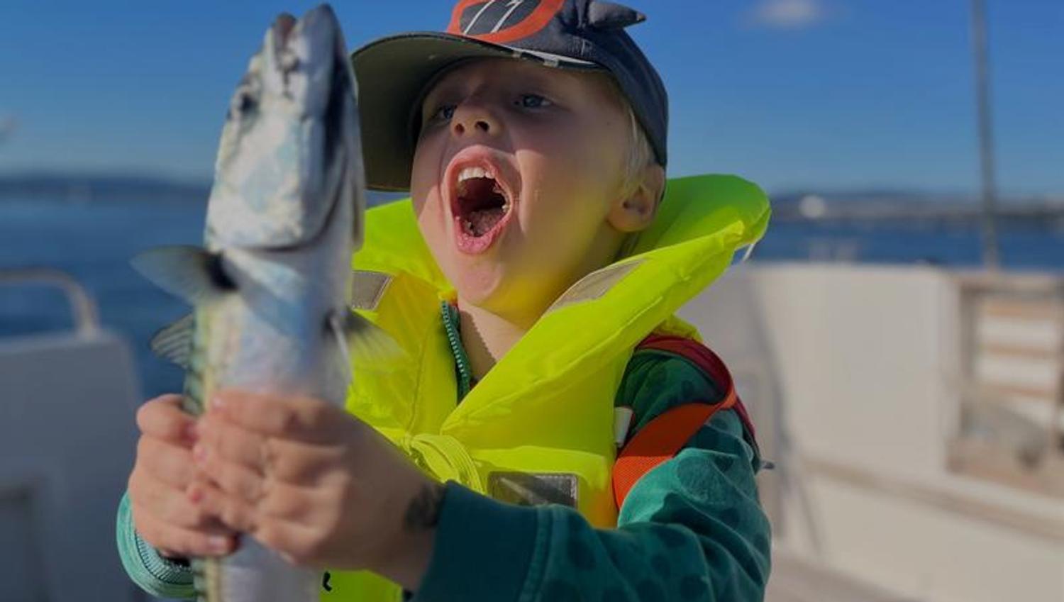 A child proudly holds up a fish they have just caught on the boat.