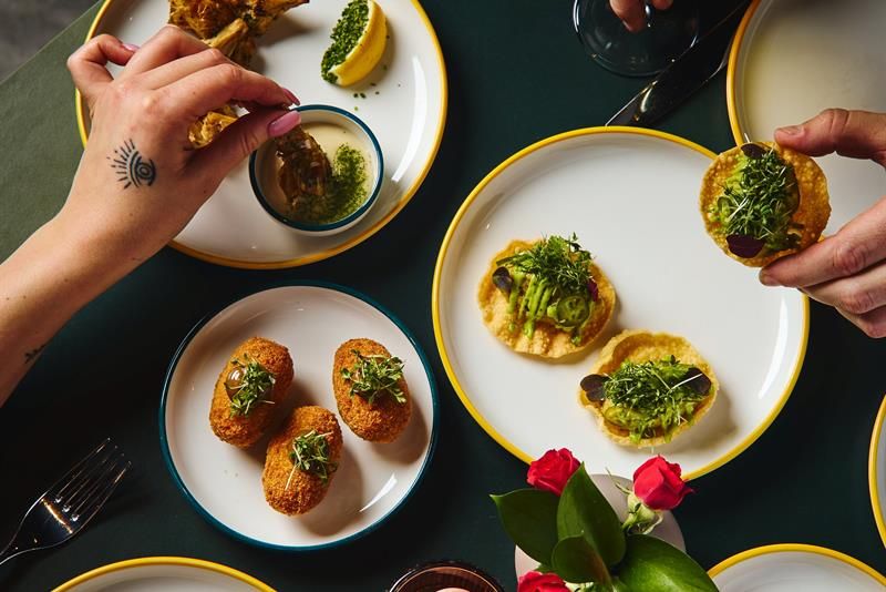 Various plates of small dishes and hands helping themselves to food from above