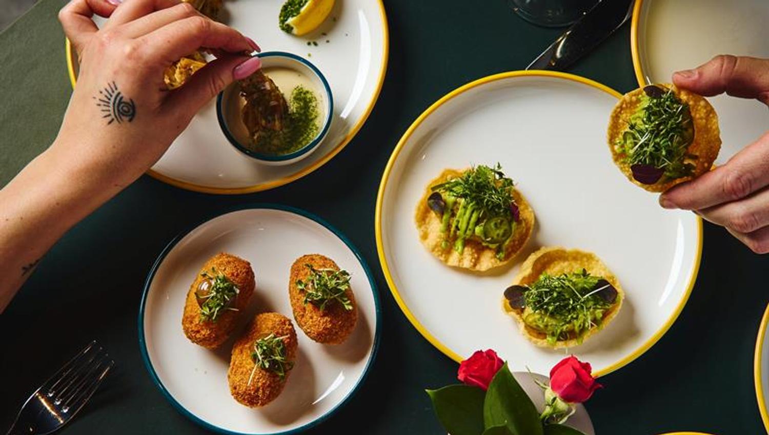 Various plates of small dishes and hands helping themselves to food from above