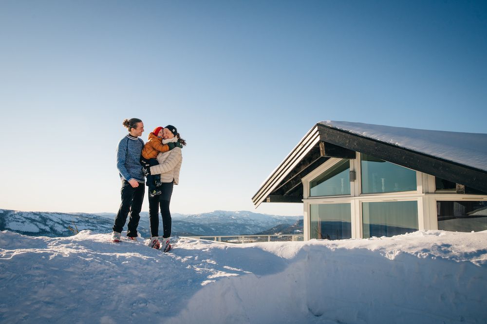 couple with child standing in front of a cabin at Lifjell Tunet in the winter 