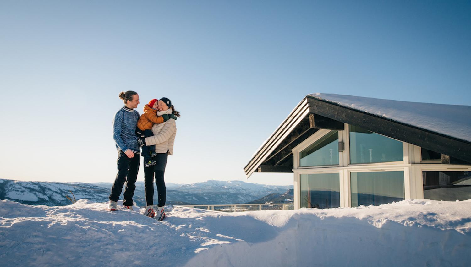 couple with child standing in front of a cabin at Lifjell Tunet in the winter
