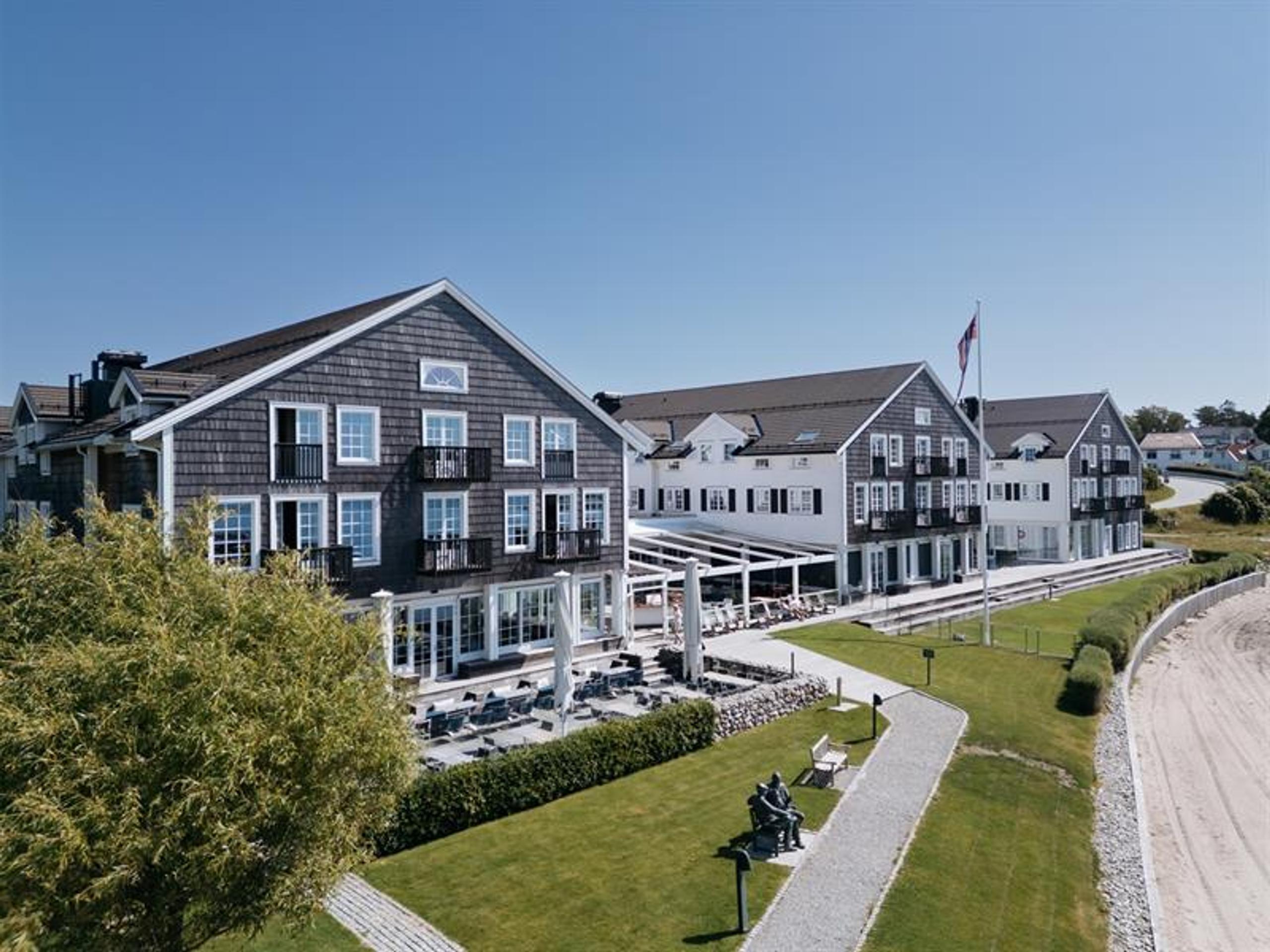 Fasade Støtvig Hotell i tre og hvite vinduer. Strand i forgrunn